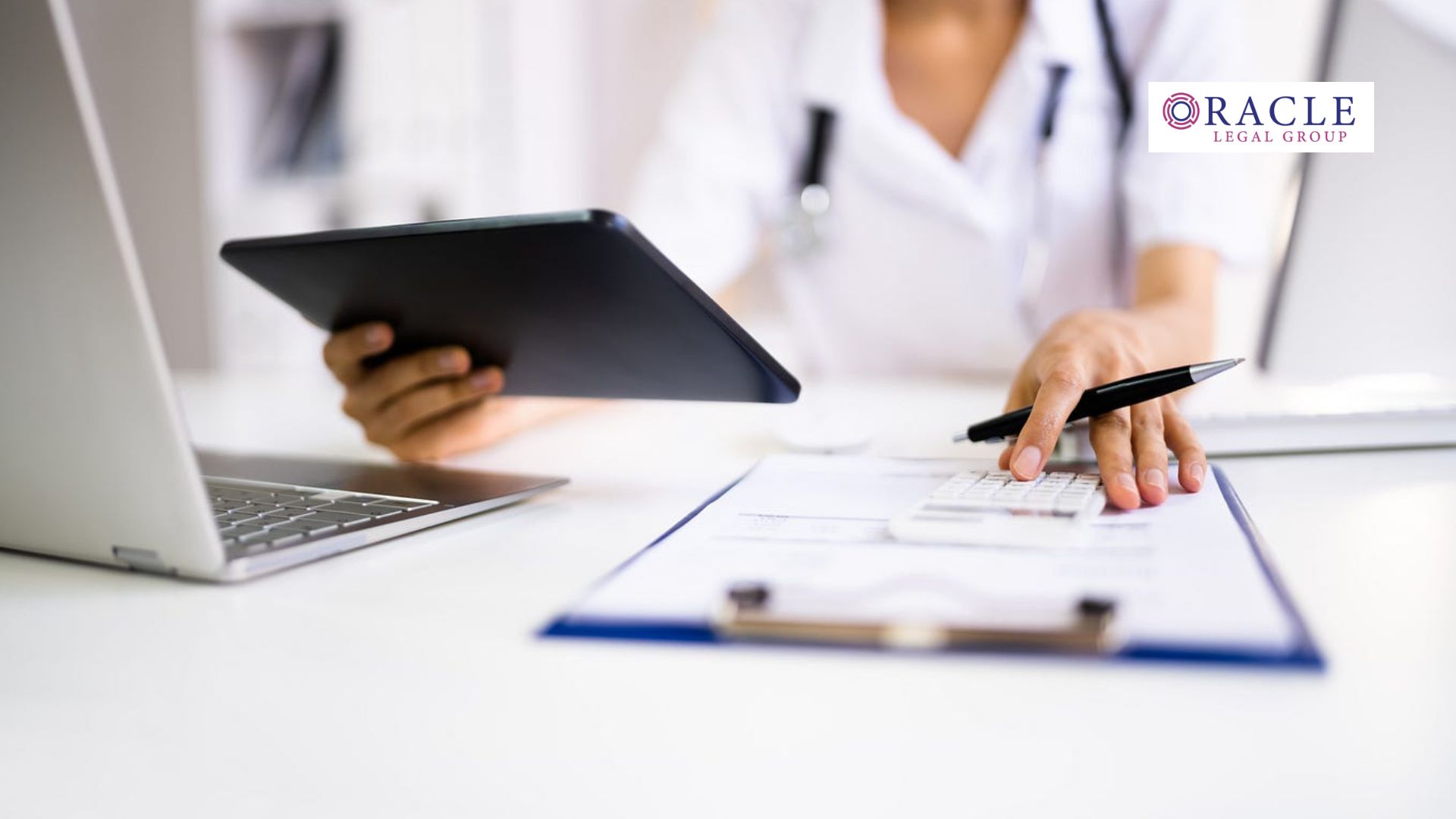 Medical professional using a tablet while reviewing documents on a clipboard at a desk, with a laptop nearby; Oracle Legal Group logo in the corner, symbolizing healthcare business operations and compliance review