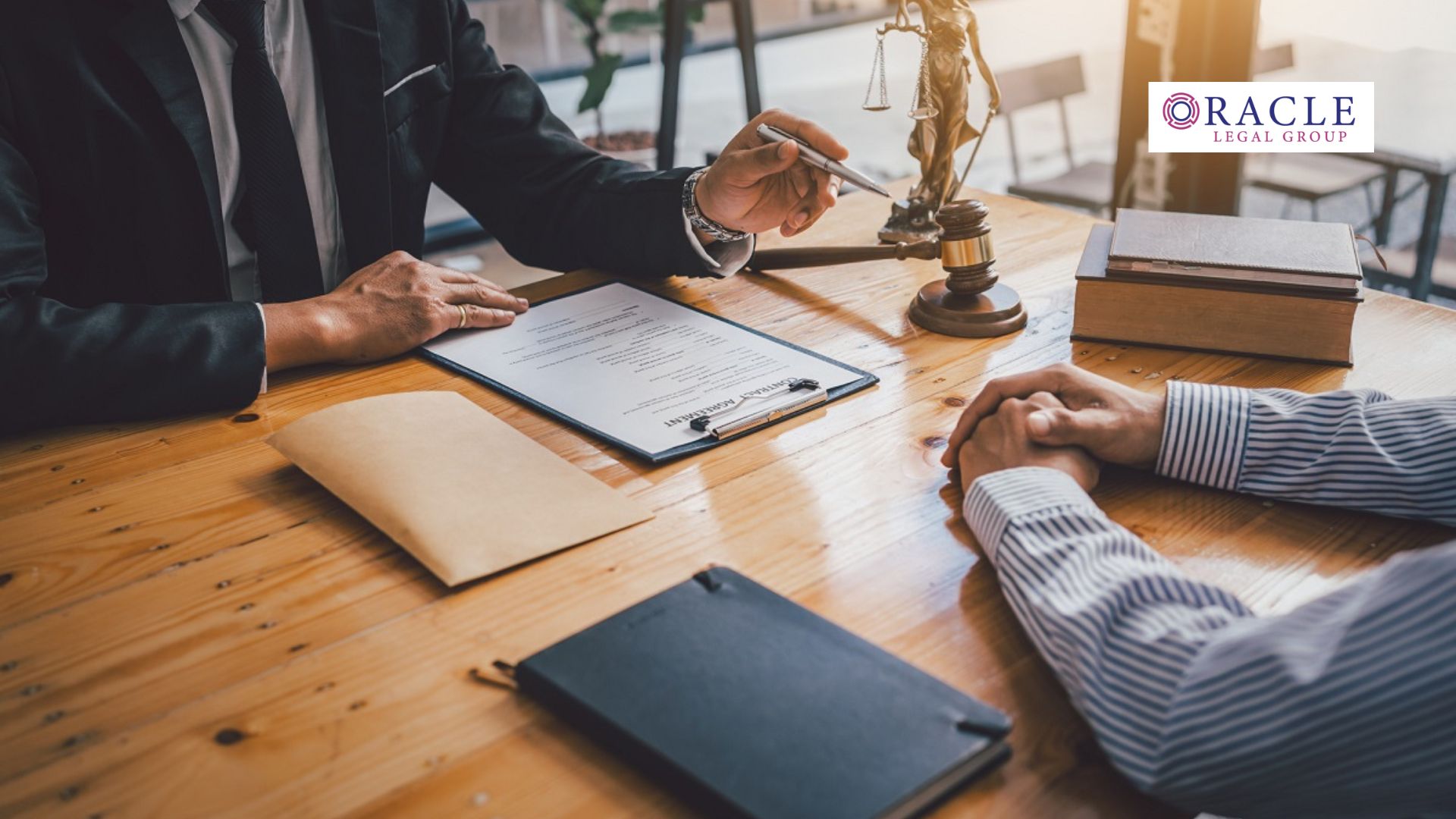 A lawyer in a suit discusses legal documents with a client across a wooden desk; visible are a gavel, legal scales, law books, and a clipboard with paperwork. The Oracle Legal Group logo is displayed in the upper right corner, emphasizing professionalism and trusted legal counsel.