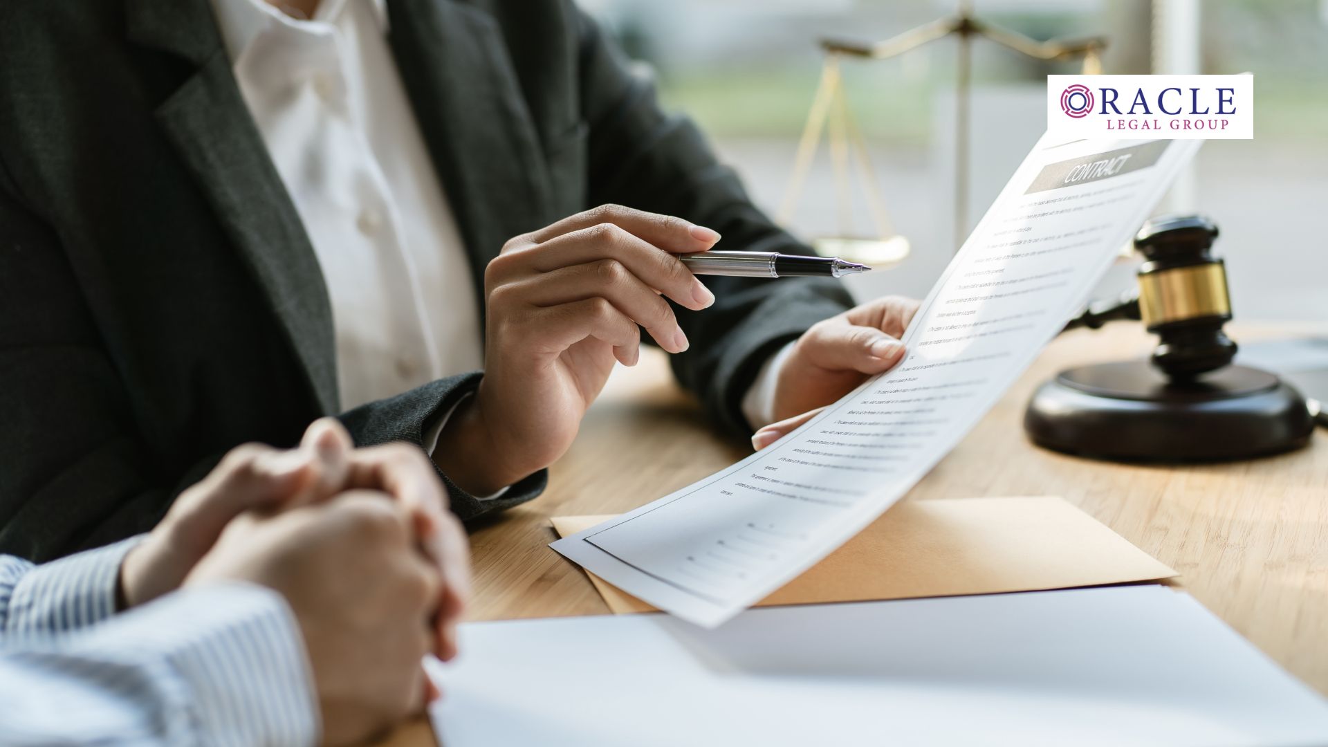 A lawyer in a dark blazer holds a pen and reviews a contract with a client across a wooden desk; a gavel and legal scales are visible in the background. The Oracle Legal Group logo is in the upper right corner, conveying authority and professional legal counsel.