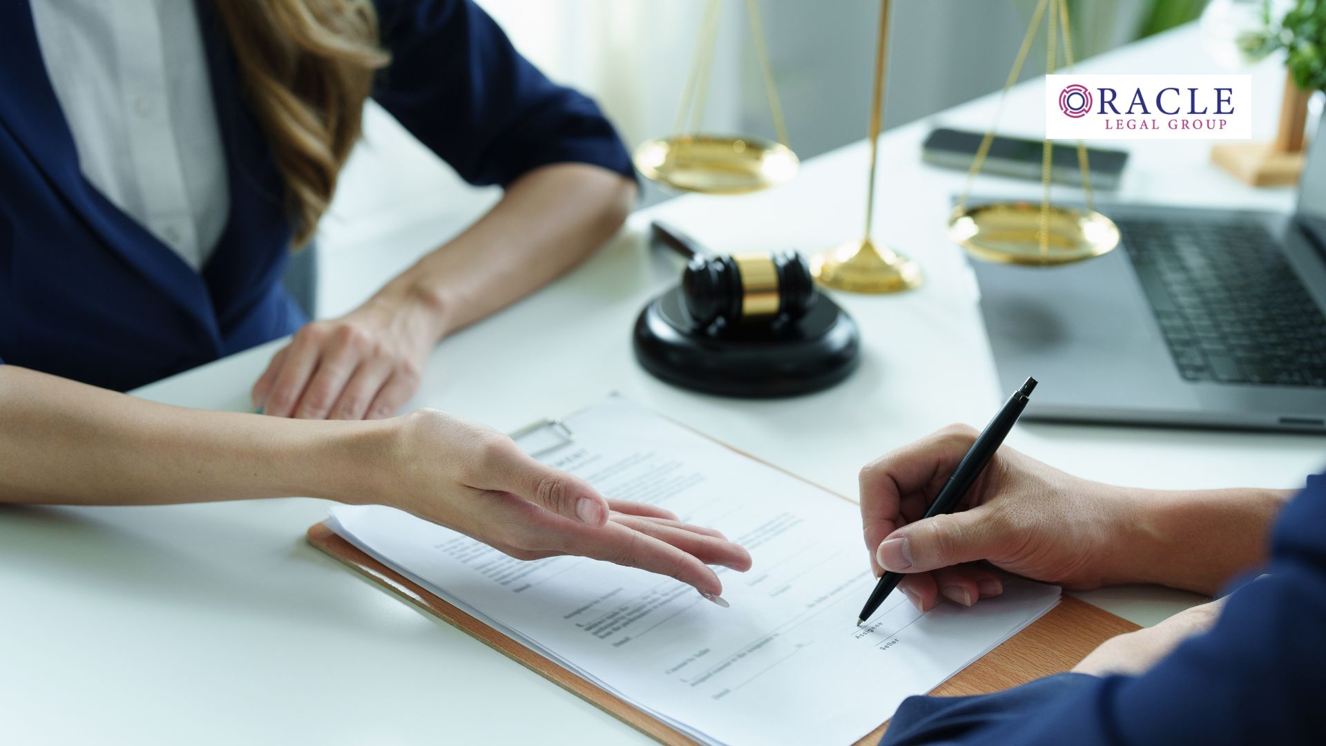 Two professionals reviewing and signing legal documents at a desk with a gavel, scales of justice, and laptop; Oracle Legal Group logo appears in the corner